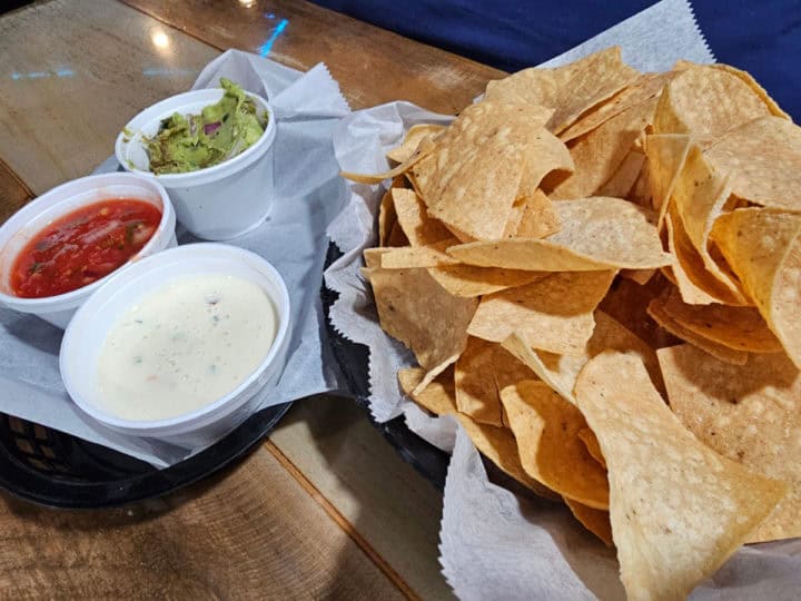 Basket of chips with a side of queso, salsa, and guacamole 