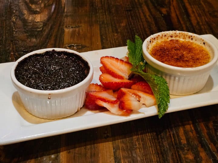 chocolate cake in a ramekin next to strawberry pieces and creme brulee in a ramekin on a white platter
