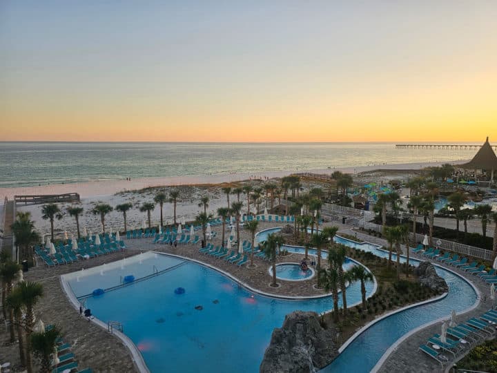 looking over a pool and lazy river to white sands and the Gulf of Mexico at sunset