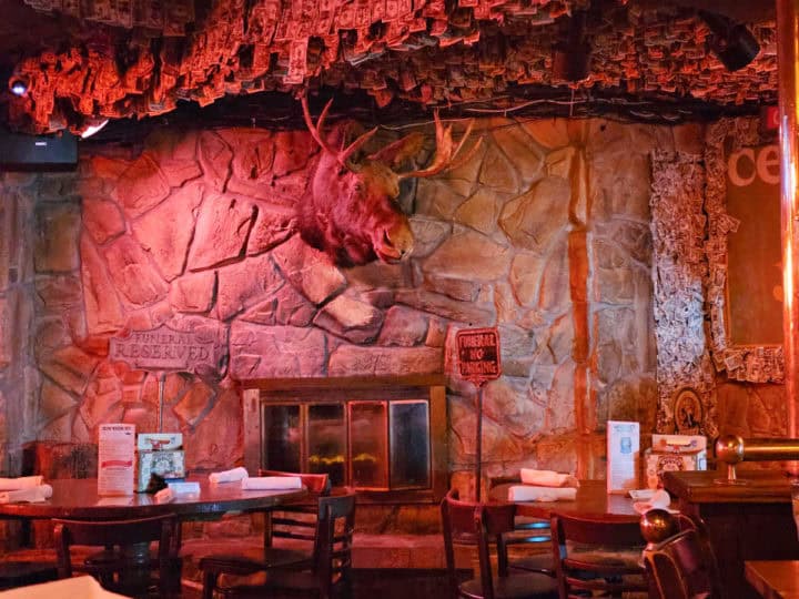 tables and chairs near a stone fireplace with a moose head over it. 