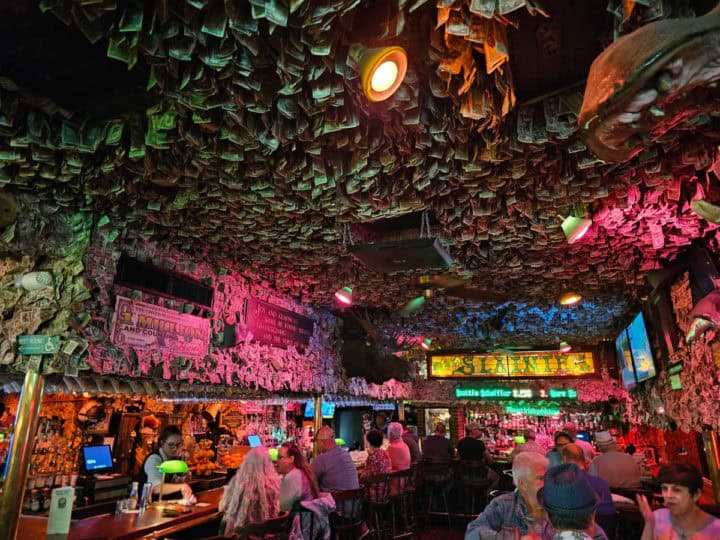 indoor bar area with people sitting at the bar, dollar bills covering every inch of the ceiling and a lot of the walls