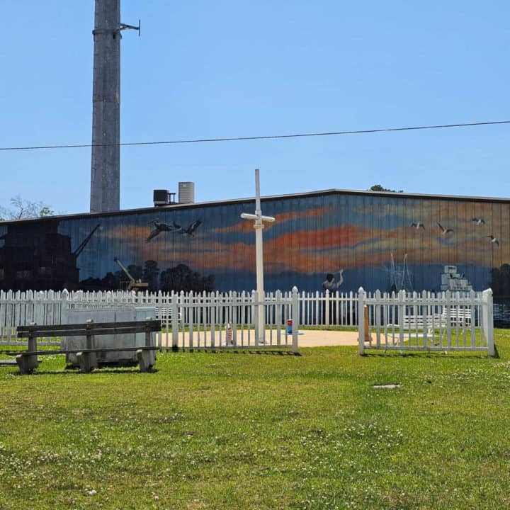 painted mural behind a fenced in park area with ship mast cross and picnic bench