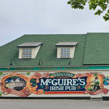 McGuire's Irish Pub mural on the side of a building with a green roof, Feasting, Imbibery & Debauchery on the side of the building above the mural.