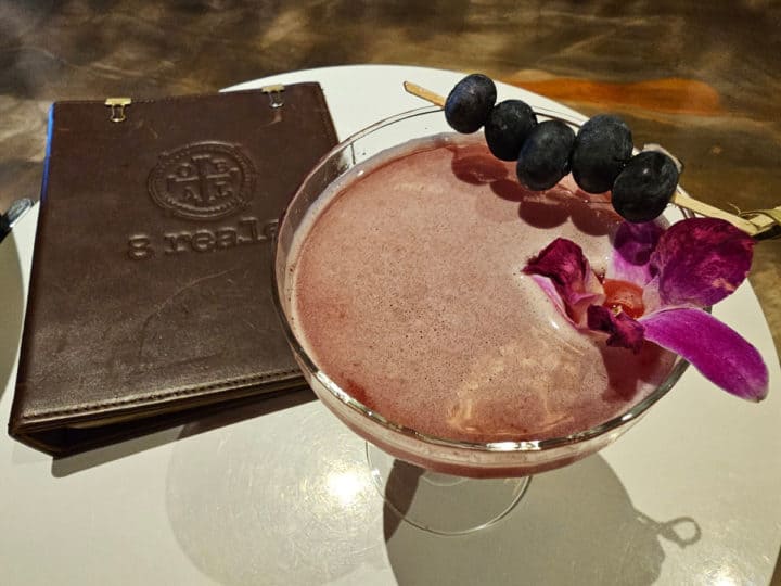 8 Reale leather bound menu next to a drink with blueberries and an orchid