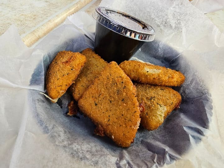 mozzarella stick wedges on a paper lined basket with a sauce cup