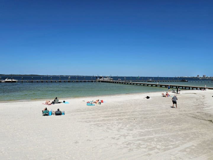 white sand beach with people relaxing, pier going out into the water