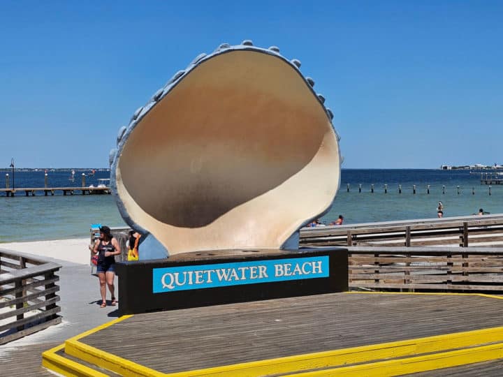 large shell sculpture above a Quietwater Beach sign with the beach in the background