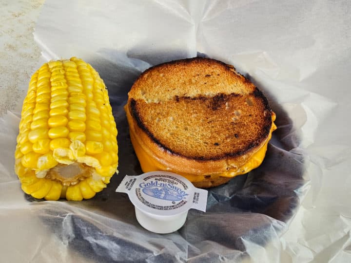 grilled cheese sandwich next to a piece of corn in a paper lined basket. 