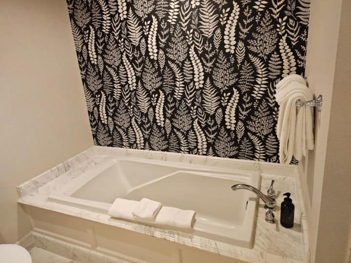 Bathtub with black and white patterned wall paper above it.