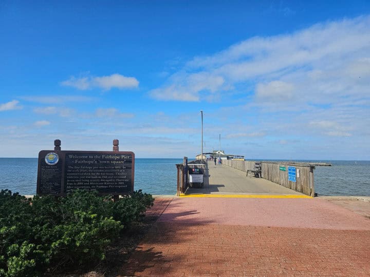 walkway leading up to the Fairhope Pier with a sign describing the piers history on a sunny day