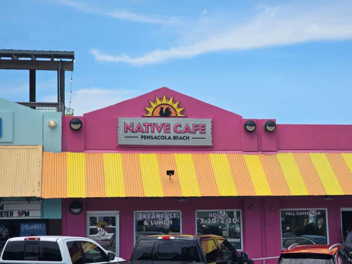Native Cafe sign on a pink and yellow building, with cars parked below