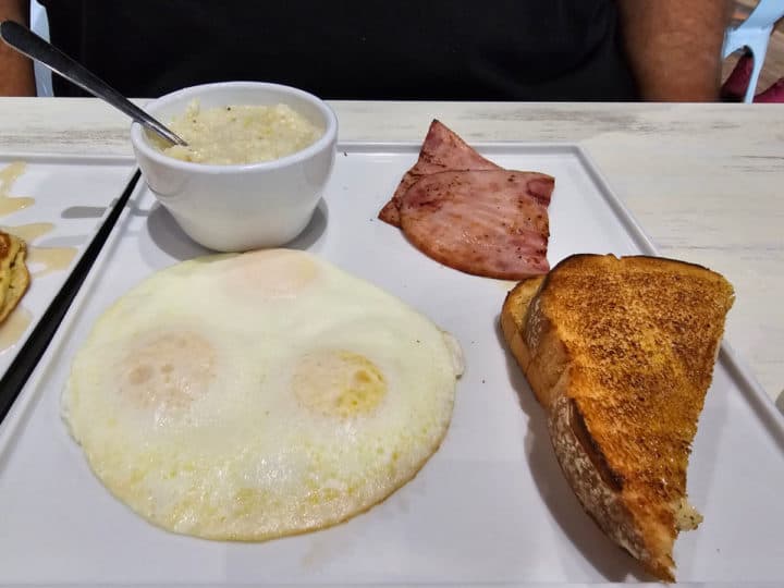3 eggs, grits, ham, and toast on a white square plate. 