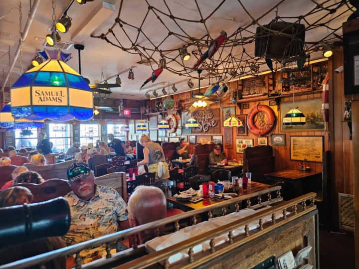 People sitting at tables and booths inside the restaurant with fishing net hanging from ceiling