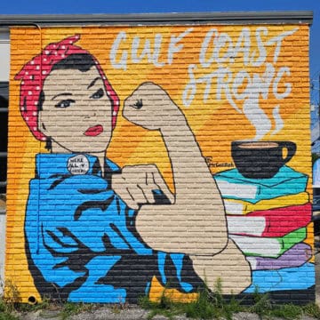 Gulf Coast strong mural with a Rosie the riveter next to a stack of books and cup of coffee