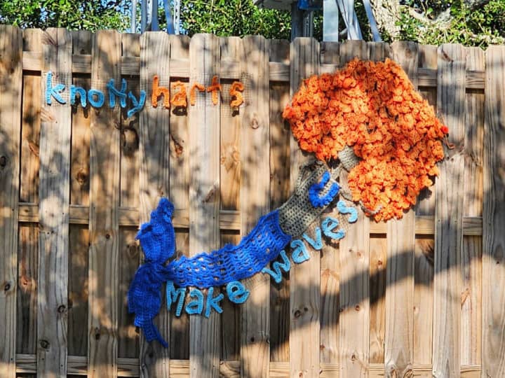 Knitted mermaid with orange hair attached to a fence