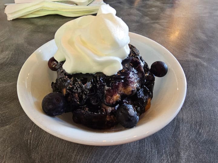 Lemon blueberry monkey bread in a small white bowl topped with whipped cream.