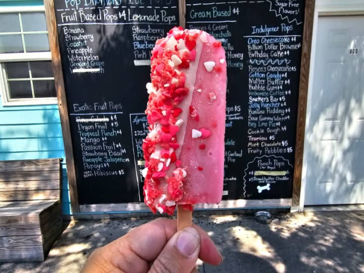 Pink popsicle with red and white heart sprinkles in front of the building and menu sign