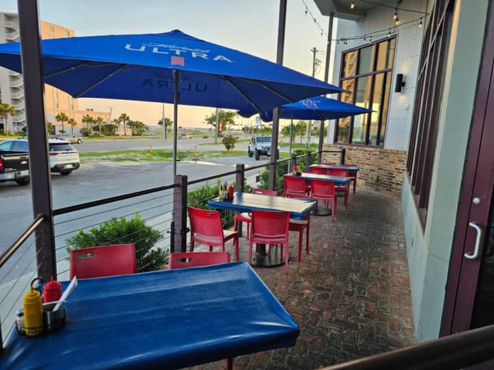 outdoor seating with blue umbrellas, with cars in a parking lot. 