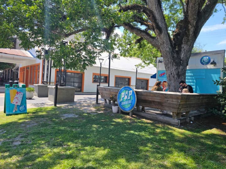 green grass leading up to a Pop Brothers logo sign and benches with people eating popsicles