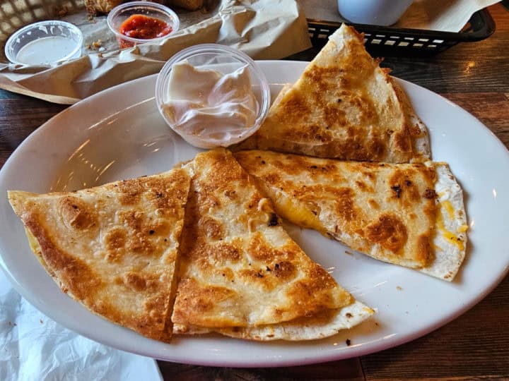 Quesadilla on a white plate with a container of sour cream. 
