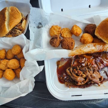 Brisket plate, pulled pork sandwich, and corn fritters in Styrofoam containers
