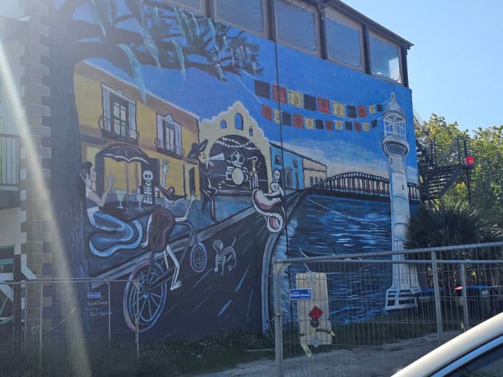 Mural on the side of a building with skeletons, margaritas, Biloxi lighthouse, and buildings 