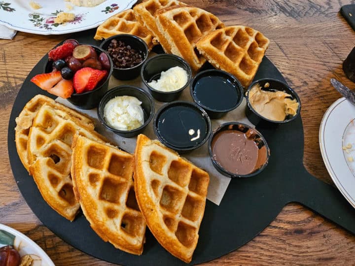 Waffle board with syrups, jams, and fresh fruit with plate nearby