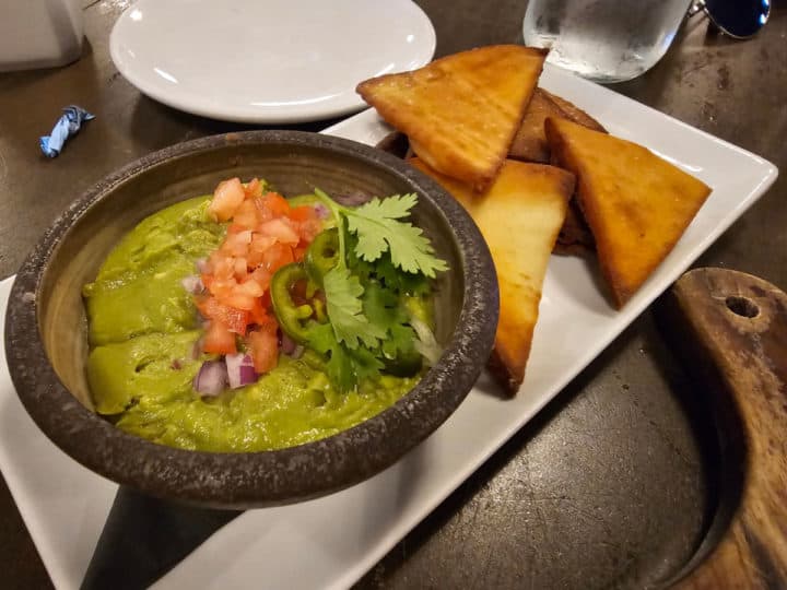 Whipped guacamole in a dark bowl next to pita chips on a white platter