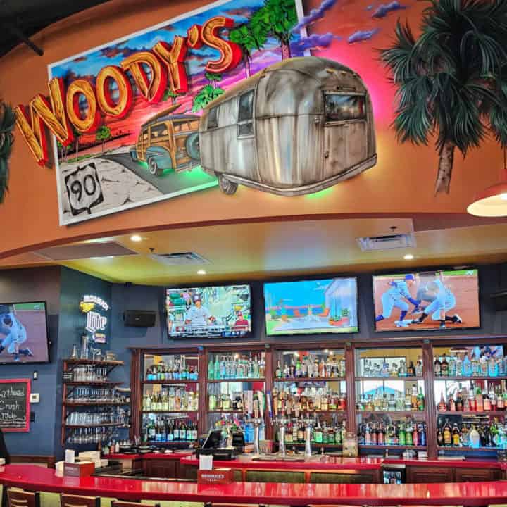 Woody's neon sign over a bar with tv's and drinks