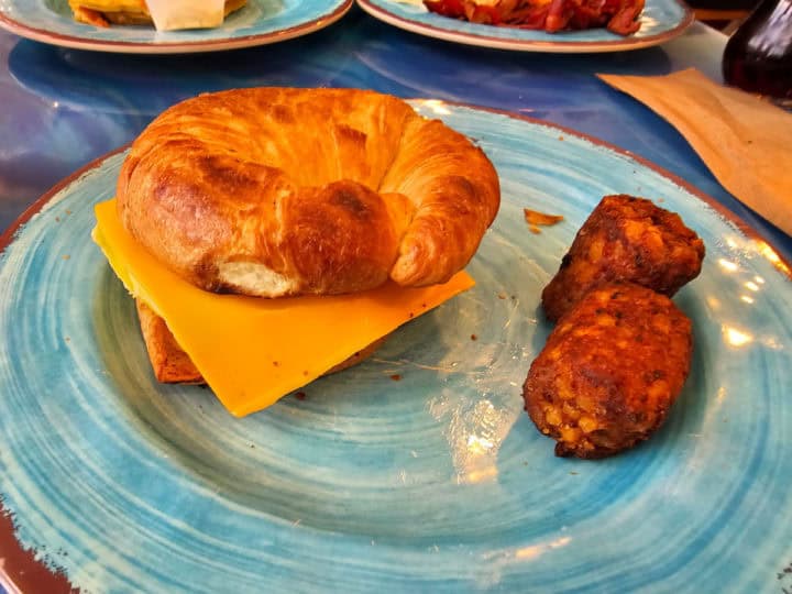 croissant breakfast sandwich with two potato rounds on a turquoise plate