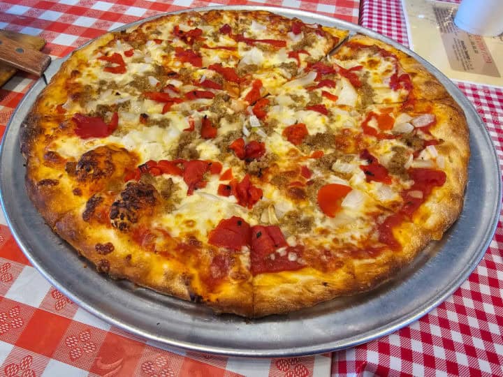 Sausage pizza on a silver pizza pan on a checkered tablecloth