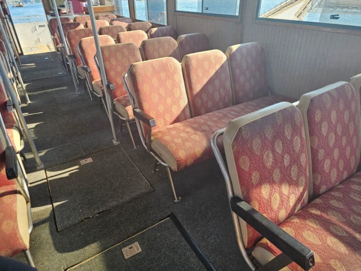 Red cloth seats inside a boat with a walkway through the middle