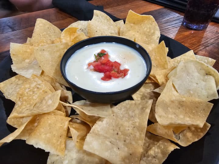 Chips and queso on a black plate with a bowl of queso in the middle