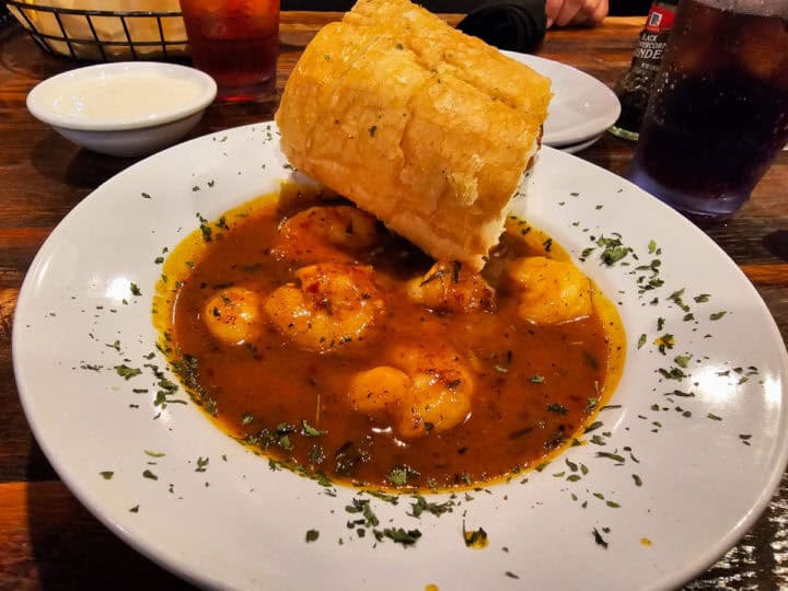 shrimp in a dark sauce in a white bowl with bread resting on the bowl 