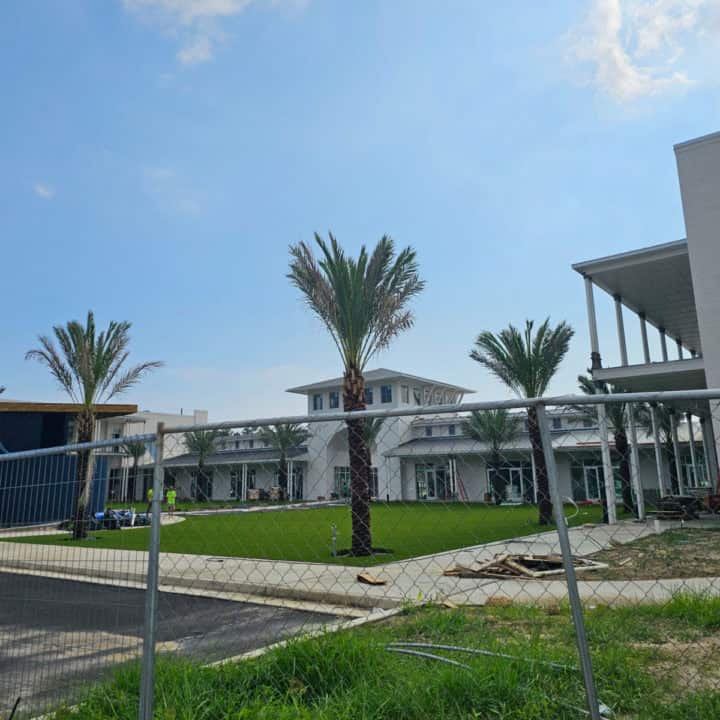 Construction fence around a white building with palm trees and people working