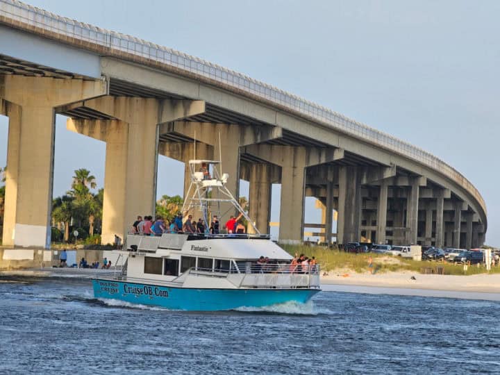 Fintatsic Boat with blue bottom and white top, people sitting on outside decks as it passes the Perdido Pass Bridge