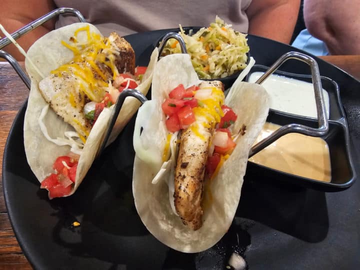 Two fish tacos in a taco stand on a black plate