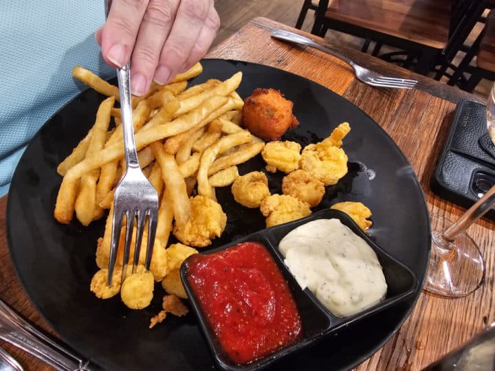 Fried shrimp platter with fries and dipping sauces on a black plate