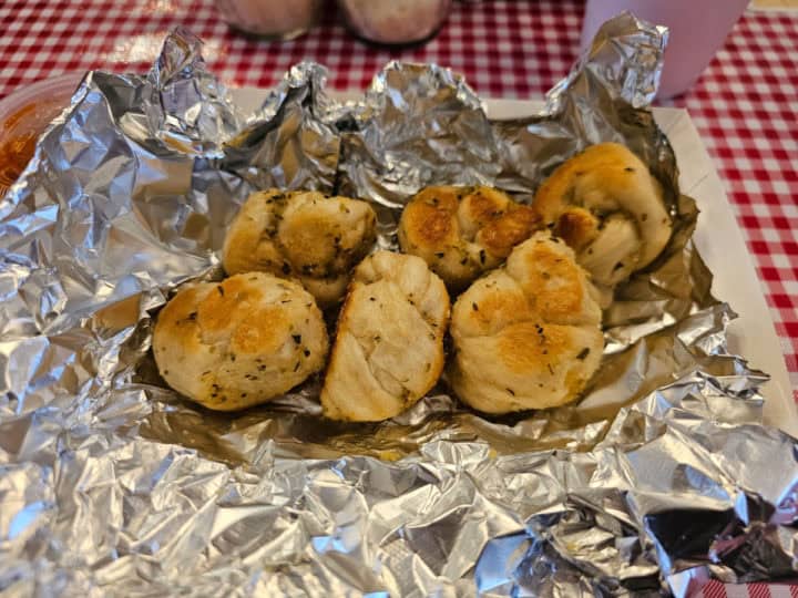 Garlic knots wrapped in aluminum foil on a checkered table cloth table 