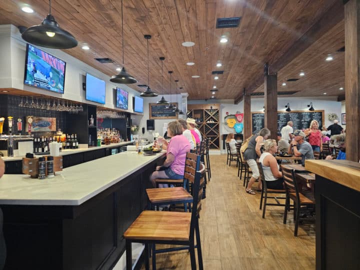 indoor bar with tall tables next to the bar, tvs on the wall, and people enjoying drinks 