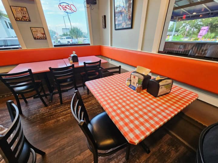 Red and white checkered table cloth covered tables with a long bench along the wall and chairs in front of the tables. 