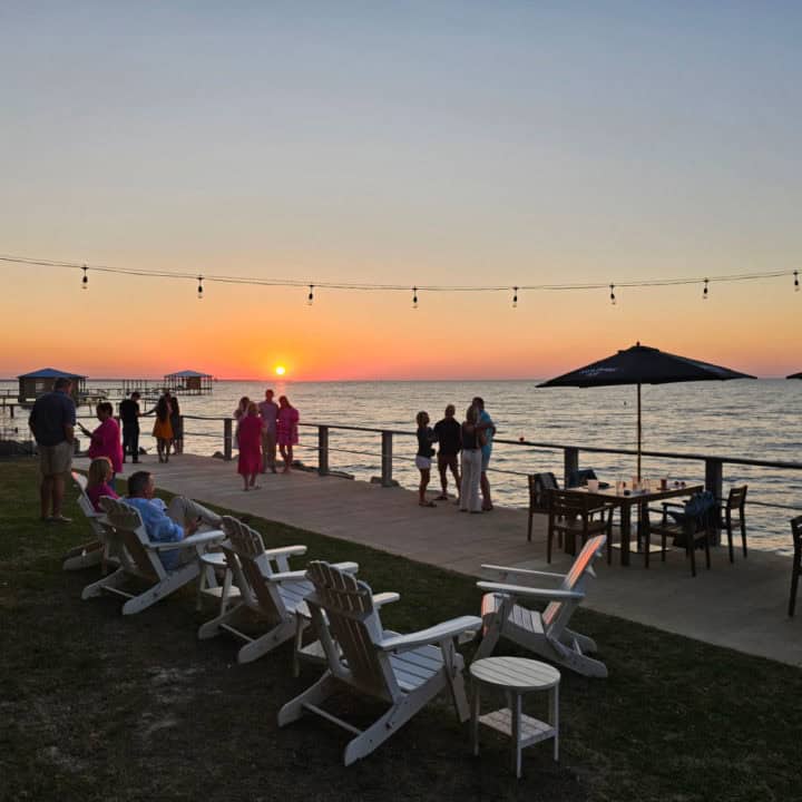 Sunset over the water looking out over Adirondack chair and tables