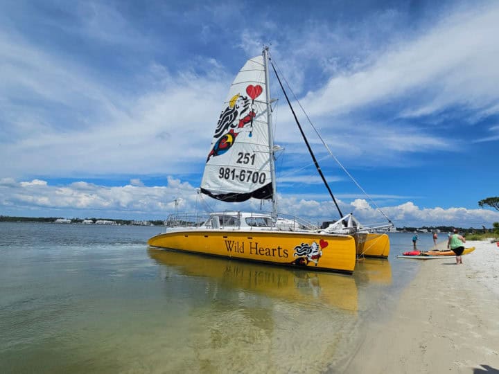 Sail Wild Hearts sailboat next to an island with blue skies and clouds in the sky