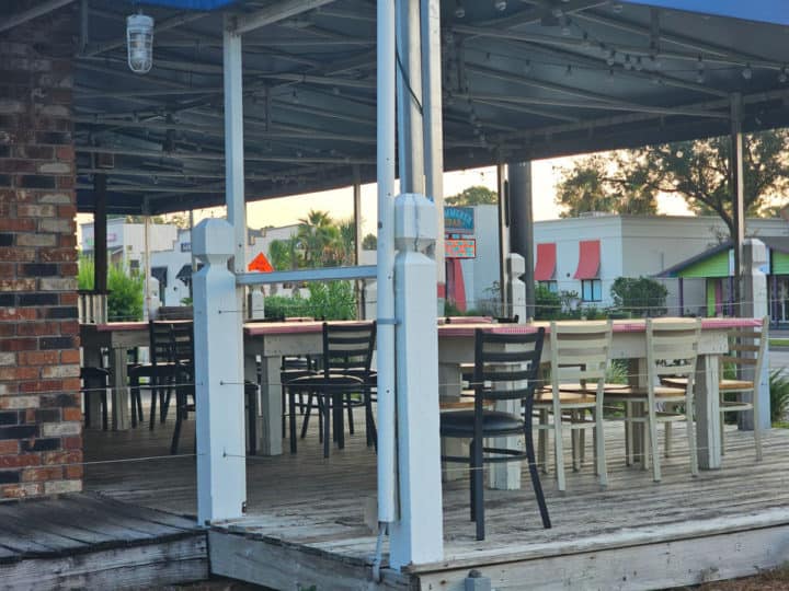 Outdoor tables and chairs on a covered wooden deck outside the restaurant. 