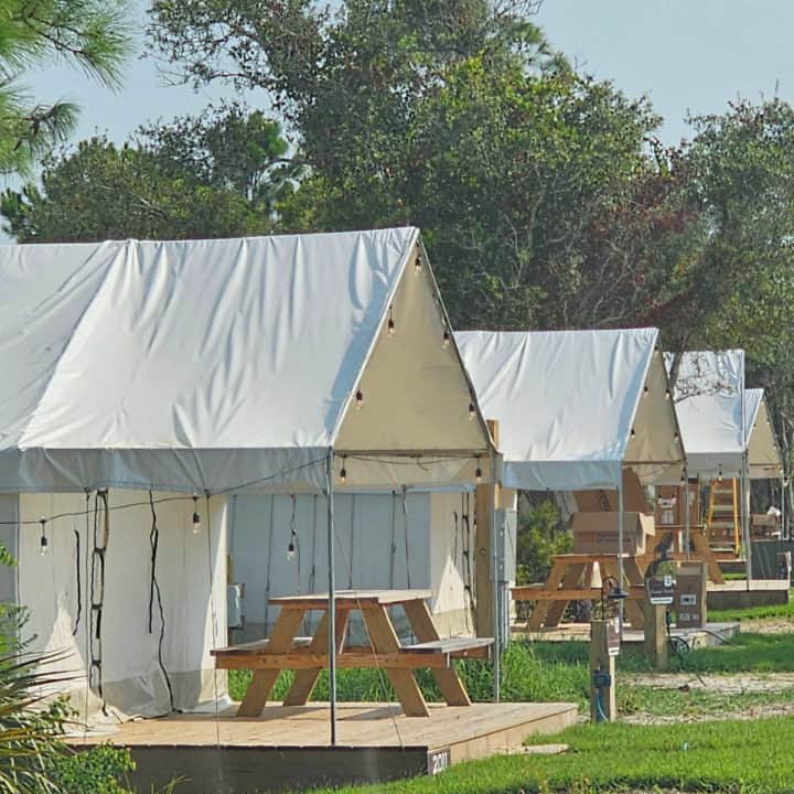 Glamping tents with picnic tables in front of them.