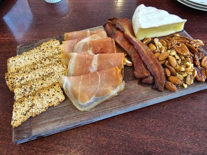 baked brie on a cutting board with bacon, proscuitto, and crackers