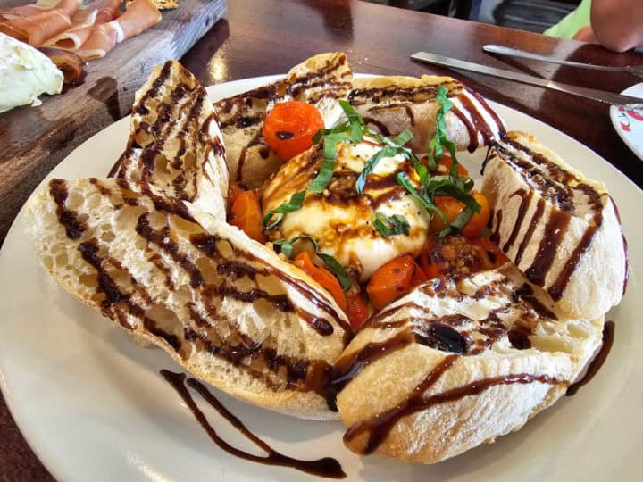 Burratta with tomatoes surrounded by baguette slices on a white plate