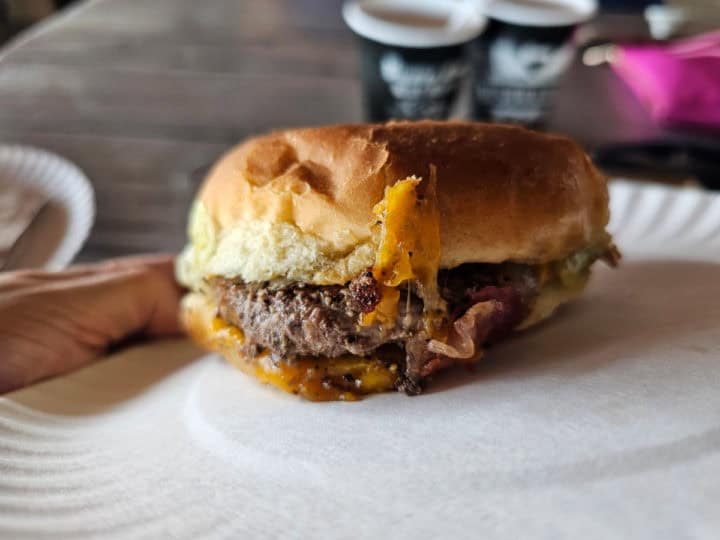 Cheeseburger on a paper plate with bushwackers in the background