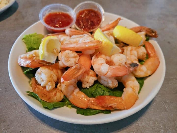 peel and eat shrimp on a white plate with two containers of cocktail sauce