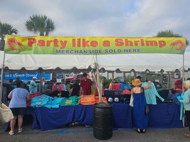 Party like a shrimp sign over a table with t-shirts and merchandise